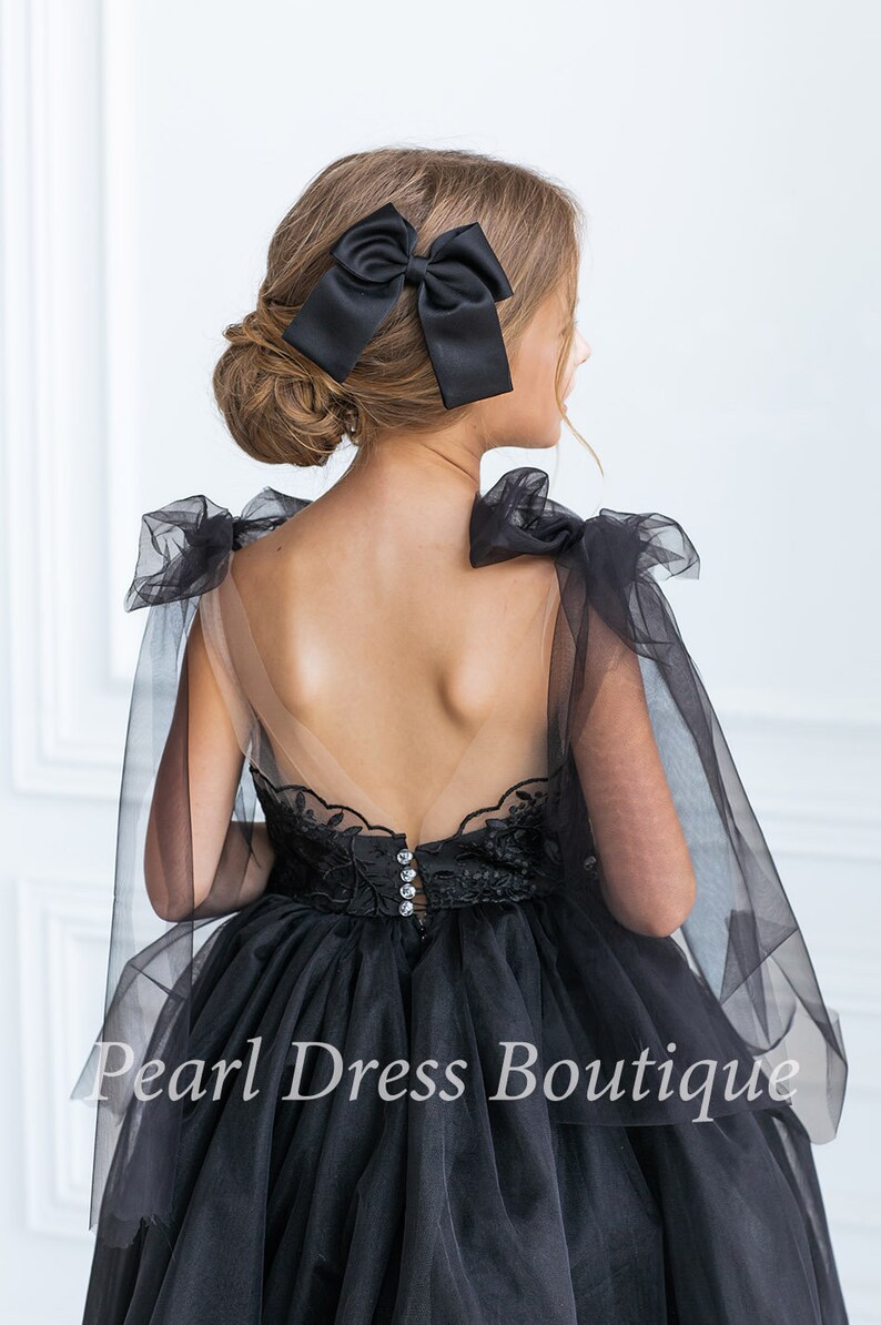 Puede incluir: Un vestido de tul negro con un corpi&ntilde;o de encaje y una espalda transparente. El vestido tiene un lazo en la espalda y una superposici&oacute;n de tul. El vestido es para una ni&ntilde;a y es perfecto para una ocasi&oacute;n especial.