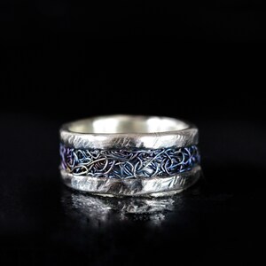May include: A silver ring with a band of woven wire in shades of blue and purple.