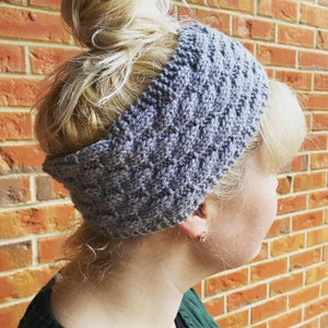 May include: A gray knitted headband with a braided pattern. The headband is worn by a person with blonde hair.