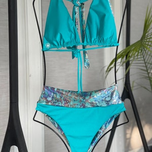 May include: A turquoise bikini top and bottom with a iridescent pattern on the bottom. The top has a halter style and ties at the neck.
