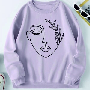 May include: A lavender sweatshirt with a black line drawing of a face with a leafy branch over one eye.