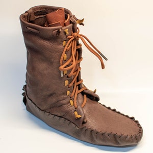 Puede incluir: Botas de cuero marr&oacute;n de estilo mocas&iacute;n con cordones y suela de cuero marr&oacute;n.