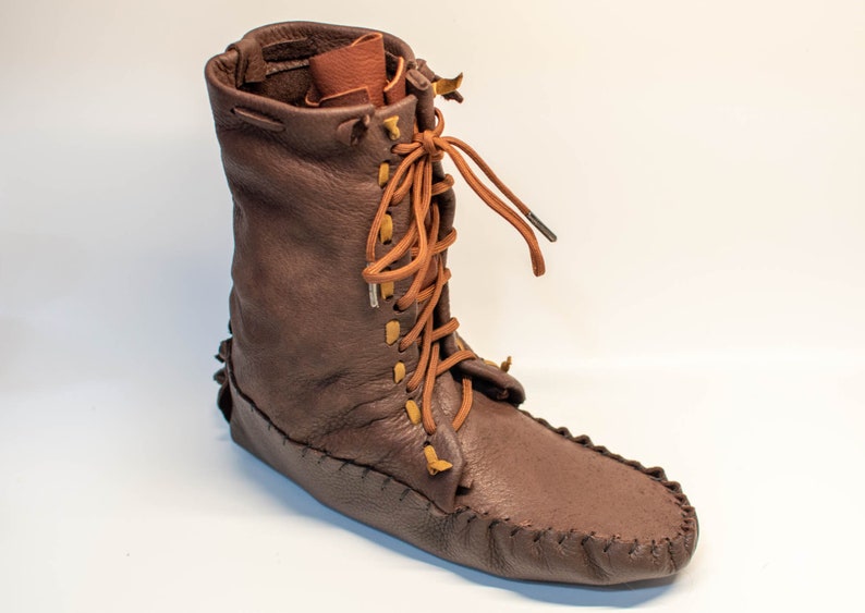 Puede incluir: Botas de cuero marr&oacute;n de estilo mocas&iacute;n con cordones y suela de cuero marr&oacute;n.