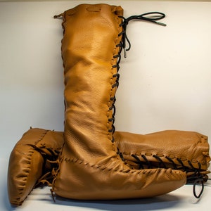 May include: A pair of brown leather boots with laces up the front. The boots are knee-high and have a pointed toe.