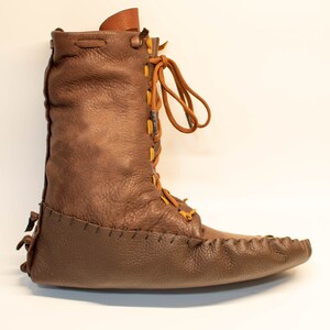 Puede incluir: Botas de mocas&iacute;n de cuero marr&oacute;n con un dise&ntilde;o de cordones y una punta puntiaguda.