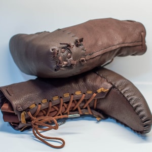 Puede incluir: Un par de botas de cuero marr&oacute;n con cordones y costuras. Las botas est&aacute;n apiladas una encima de la otra.