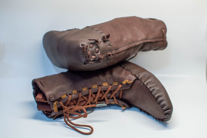 Puede incluir: Un par de botas de cuero marr&oacute;n con cordones y costuras. Las botas est&aacute;n apiladas una encima de la otra.