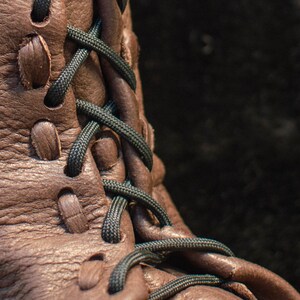 Puede incluir: Primer plano de una bota de cuero marr&oacute;n con cordones negros. Los cordones est&aacute;n atados en un patr&oacute;n de cruz.