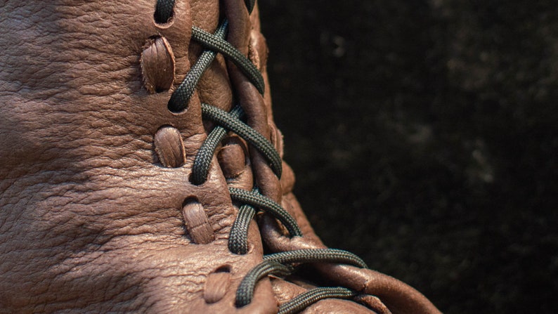 Puede incluir: Primer plano de una bota de cuero marr&oacute;n con cordones negros. Los cordones est&aacute;n atados en un patr&oacute;n de cruz.