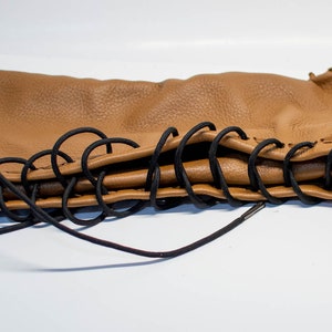 May include: A brown leather boot with black laces. The boot is folded in half and the laces are tied together.