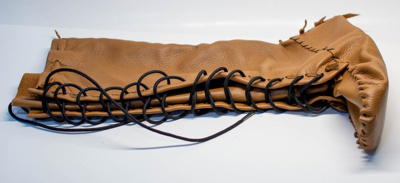 May include: A brown leather boot with black laces. The boot is folded in half and the laces are tied together.