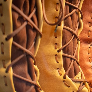 May include: Close-up of four pairs of brown leather boots with laces. The boots are all different shades of brown and have a rustic look.