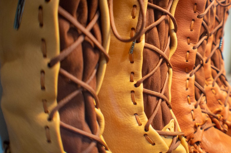 May include: Close-up of four pairs of brown leather boots with laces. The boots are all different shades of brown and have a rustic look.