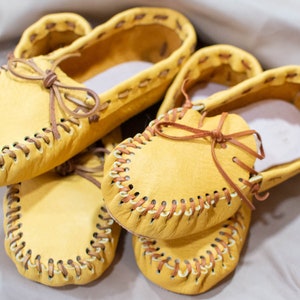 May include: Three pairs of yellow leather moccasins with brown stitching and laces.