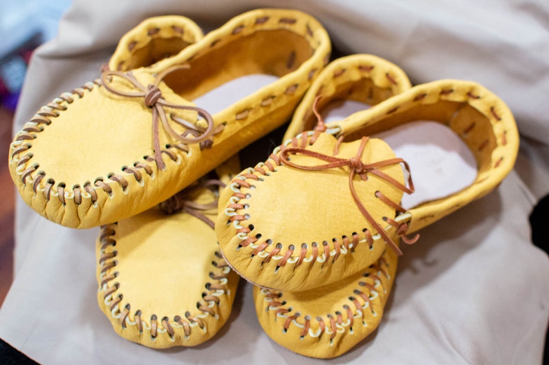 May include: Three pairs of yellow leather moccasins with brown stitching and laces.