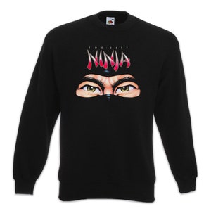 Pode incluir: Camisola de manga comprida preta com uma estampa gráfica de olhos de ninja e o texto "The Last Ninja".
