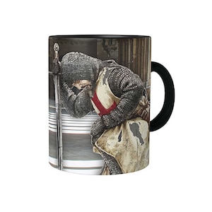 May include: A black and white mug with a design of a knight in armor kneeling with his head bowed. The knight is wearing a red cross on his chest and is holding a sword. The mug has a black handle.