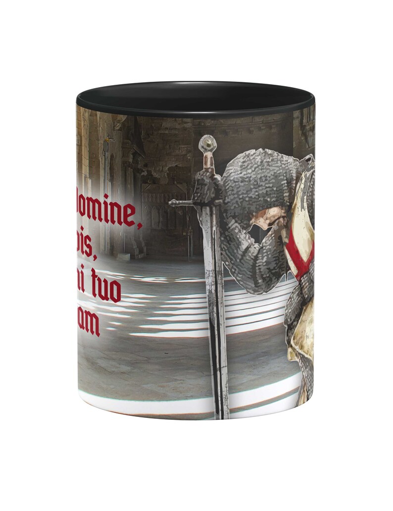 May include: A black ceramic mug with a white interior. The mug features a graphic of a knight in armor kneeling with a sword. The knight is wearing a red and white cross on his chest. The text "Domine, bis, ni tuo am" is printed in red on the mug.