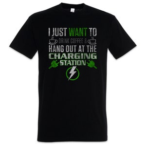 Peut inclure: T-shirt noir avec l'inscription "I JUST WANT TO DRINK COFFEE & HANG OUT AT THE CHARGING STATION". Le motif comprend des tasses à café, des prises de recharge et un éclair.