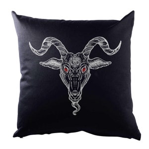 Könnte beinhalten: Schwarzes quadratisches Kissen mit einer weißen Illustration eines Ziegenkopfes mit großen, gebogenen Hörnern und roten Augen. Der Ziegenkopf hat ein drittes Auge in der Mitte der Stirn. Dekorativer Artikel.