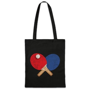 Könnte beinhalten: Eine schwarze Tragetasche mit einem Vintage-Design aus zwei gekreuzten Tischtennis-Schlägern und einem Ball. Die Schläger sind rot und blau.