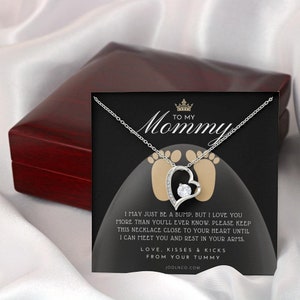 May include: A silver necklace with a heart pendant featuring a small clear stone. The necklace is in a black box with a message that reads "To My Mommy I may just be a bump, but I love you more than you'll ever know. Please keep this necklace close to your heart until I can meet you and rest in your arms. Love, Kisses & Kicks From Your Tummy" and the website address "JOOLNCO.COM".