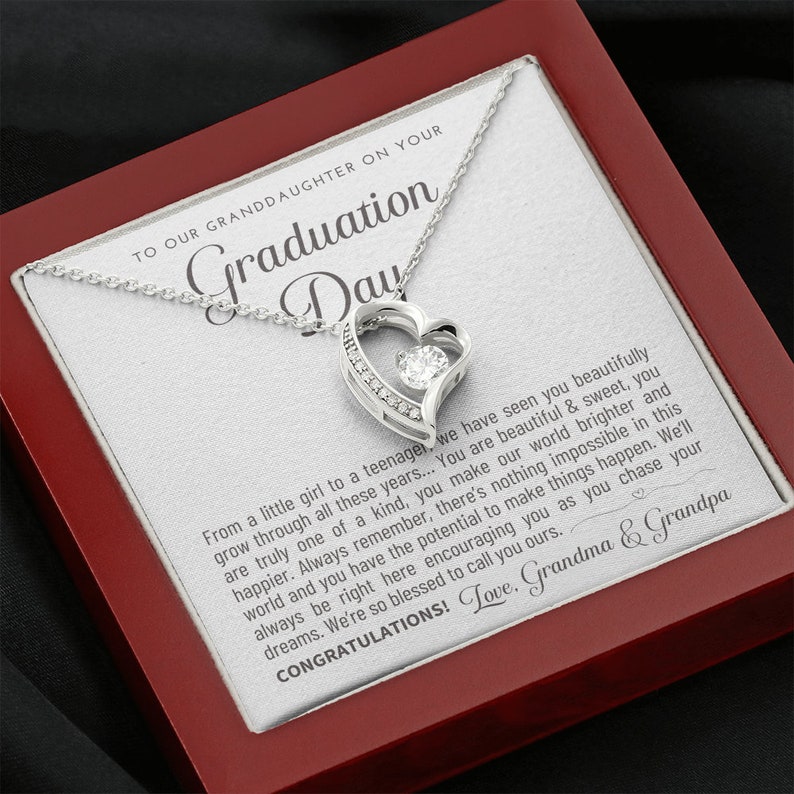 Peut inclure: Un collier pendentif argent&eacute; en forme de c&oelig;ur avec une pierre centrale transparente, pr&eacute;sent&eacute; dans un coffret rouge. Le coffret contient un message imprim&eacute; pour une petite-fille le jour de sa remise de dipl&ocirc;me.