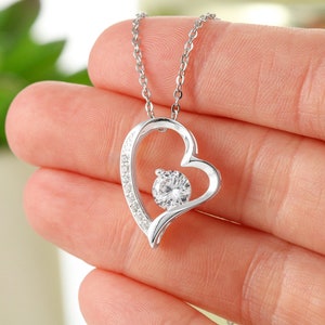 May include: Silver necklace with a heart-shaped pendant featuring a sparkling clear stone in the center. The heart is outlined with smaller clear stones.