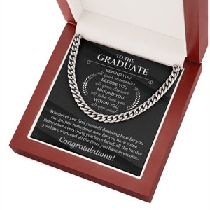 Pu&ograve; includere: Una placca nera con una collana a catena argentata all'interno di una scatola di legno rossa. La placca riporta le parole "To the Graduate" e un messaggio su tutti i ricordi, i sogni e l'amore che circondano il laureato.