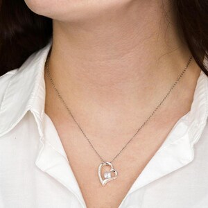 May include: A silver necklace with a heart-shaped pendant featuring a small, clear gemstone in the center. The heart is open on one side, creating a delicate and romantic look.