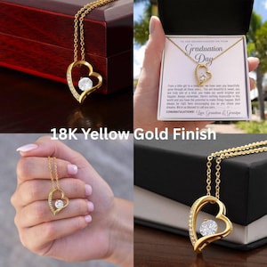 Peut inclure: Un collier pendentif en forme de c&oelig;ur dor&eacute; avec une pierre centrale en cristal transparent. Le collier est pr&eacute;sent&eacute; dans un coffret cadeau avec un message pour une petite-fille pour son jour de remise de dipl&ocirc;me. Le texte "18K Yellow Gold Finish" est &eacute;galement visible.
