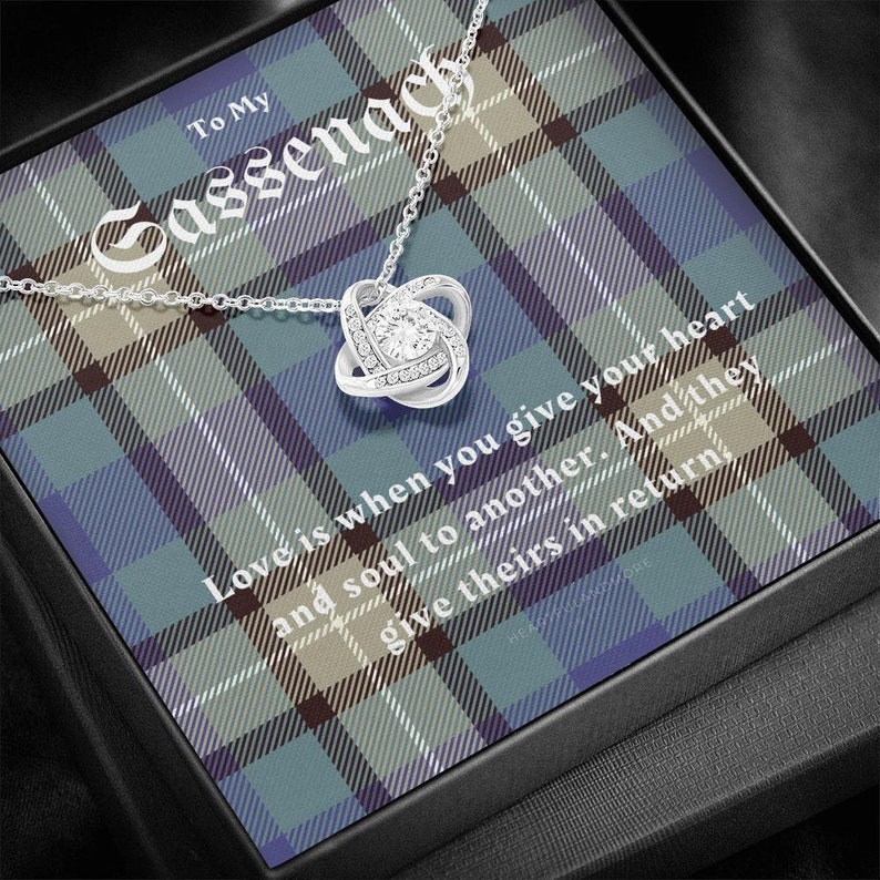 Pode incluir: Um colar com pingente de n&oacute; prateado com uma pedra central brilhante, apresentado numa caixa de presente. A caixa apresenta um padr&atilde;o xadrez em tons de azul, verde e castanho, com o texto "To My Sassenach". A inscri&ccedil;&atilde;o diz "Amor &eacute; quando voc&ecirc; d&aacute; seu cora&ccedil;&atilde;o e alma a outro."