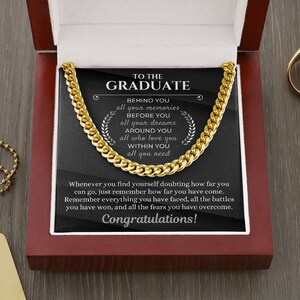 Pu&ograve; includere: Una collana a catena d'oro in una scatola di velluto rosso con sfondo nero. La scatola contiene un messaggio per un laureato che recita "To the Graduate" e include il testo "Behind you all your memories, Before you all your dreams, Around you all who love you, Within you all you need." Il messaggio termina con "Congratulations!"