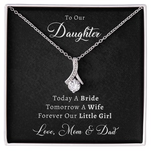 May include: A silver necklace with a clear crystal pendant in a black gift box. The box has the text "To Our Daughter Today A Bride Tomorrow A Wife Forever Our Little Girl Love, Mom & Dad" printed on it.