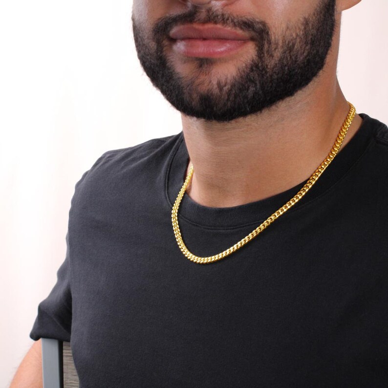 Pu&ograve; includere: Una collana a catena d'oro con uno stile a maglie a curb. La catena &egrave; indossata da una persona con la barba e una maglietta nera.