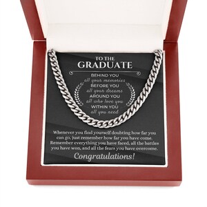 Pu&ograve; includere: Una collana a catena d'argento in una scatola rossa con sfondo nero. Il testo sullo sfondo recita "To the Graduate" e include un messaggio motivazionale sul ricordare quanto sei arrivato lontano.
