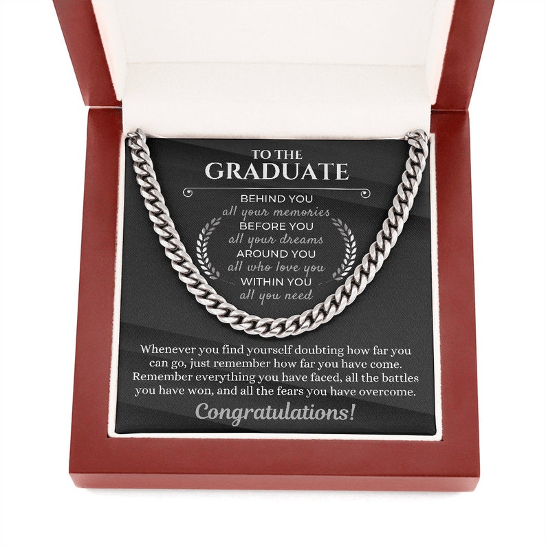 Pu&ograve; includere: Una collana a catena d'argento in una scatola rossa con sfondo nero. Il testo sullo sfondo recita "To the Graduate" e include un messaggio motivazionale sul ricordare quanto sei arrivato lontano.