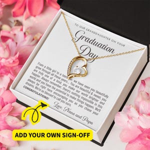Peut inclure: Un collier pendentif en forme de c&oelig;ur dor&eacute; avec une pierre pr&eacute;cieuse transparente, pr&eacute;sent&eacute; dans un coffret cadeau blanc. La bo&icirc;te contient un message pour une petite-fille pour son jour de remise de dipl&ocirc;me. Fleurs roses en arri&egrave;re-plan.