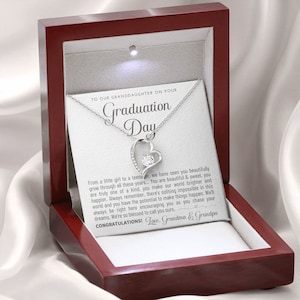 Peut inclure: Un collier en argent avec un pendentif en forme de c&oelig;ur orn&eacute; d'une pierre pr&eacute;cieuse transparente est pr&eacute;sent&eacute; dans un coffret &agrave; bijoux en bois rouge ouvert. Le coffret contient une carte blanche avec le texte "To our Granddaughter on your Graduation Day."