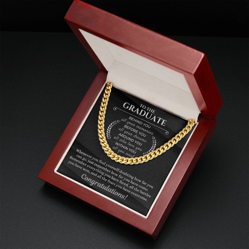Pu&ograve; includere: Una collana a catena dorata in una scatola di legno con una placca nera che recita "To the Graduate" e un messaggio su ricordi, sogni e amore.