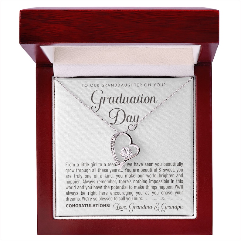 Peut inclure: Un collier en argent avec un pendentif en forme de c&oelig;ur, pr&eacute;sent&eacute; dans un coffret &agrave; bijoux rouge fonc&eacute;. Le pendentif comporte une pierre pr&eacute;cieuse centrale et l'inscription "Graduation Day" et un message.