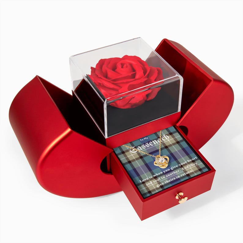 Pode incluir: Uma caixa de presente vermelha em forma de cora&ccedil;&atilde;o com uma rosa vermelha preservada em uma caixa transparente. Dentro, uma gaveta revela um colar em um cart&atilde;o xadrez com o texto "To My Gassenach".