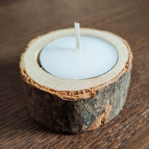 Pode incluir: Um porta-velas de madeira com uma vela de chá branca dentro. O porta-velas é feito de um galho de árvore natural e tem um aspecto rústico.