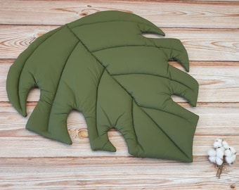 May include: A large, green, quilted leaf-shaped play mat. The mat is made of soft fabric and has a textured surface.