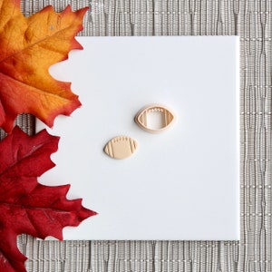 Puede incluir: Dos cortadores de galletas de plástico con forma de balón de fútbol americano. Los cortadores están sobre una superficie blanca.