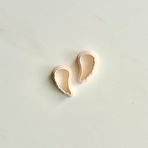 Puede incluir: Dos cortadores de galletas de plástico blanco en forma de alas de ángel.