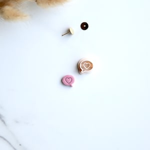 May include: A pair of pink and brown heart-shaped chat bubble earrings. The earrings are made of polymer clay and have a glossy finish.