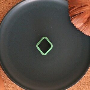 May include: A green diamond-shaped cookie cutter on a black plate. The plate is on a cork surface.