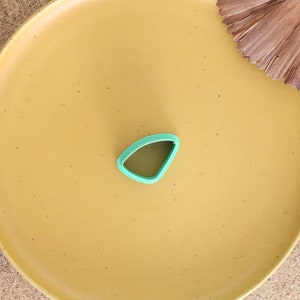 May include: A green plastic cookie cutter shaped like a triangle on a yellow plate.