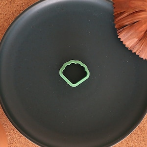 May include: A green plastic cookie cutter shaped like a seashell on a black plate.